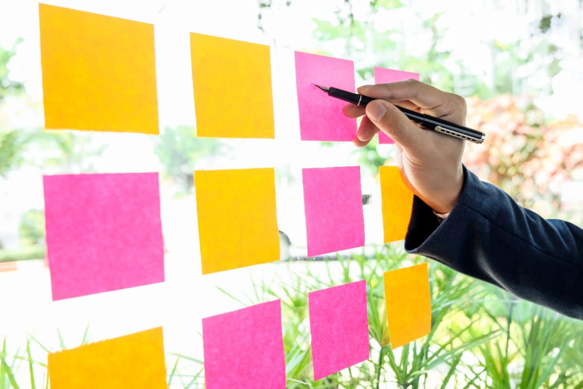 Hand die gele en roze plaknotities op een glazen wand plakt tijdens het uitwerken van een contentstrategie